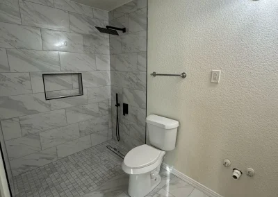 Modern bathroom with a walk-in shower, white tiles, toilet, towel rack, and hookups for a washer or sink.