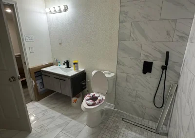 Modern bathroom with a wall-mounted sink, open shower, and toilet with a floral seat cover.