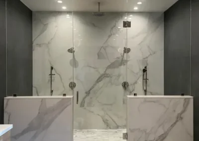 Modern marble shower with glass doors, dual showerheads, and grey-black accent walls under recessed lighting.