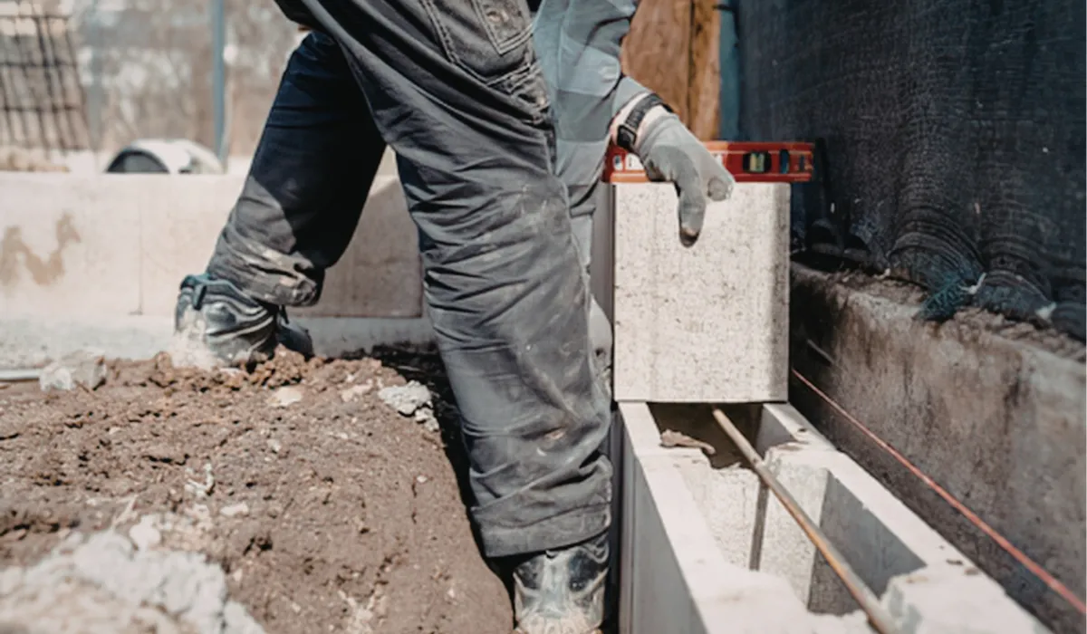 A construction worker lays a concrete block with a level tool at a building site.