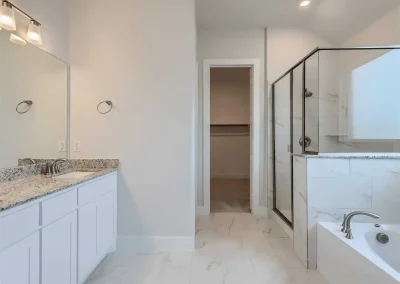 Modern bathroom with white cabinets, granite countertop, glass shower, bathtub, and marble tile floor.