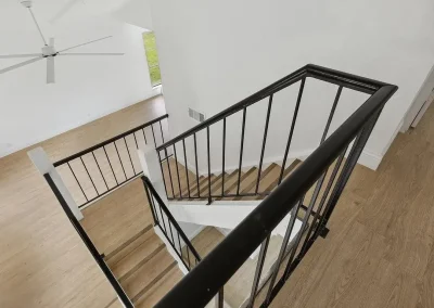 View from the top of a wooden staircase with black railings in a bright, modern home with white walls.