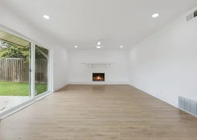 Bright living room with wood flooring, white walls, fireplace, and large sliding glass door to backyard.