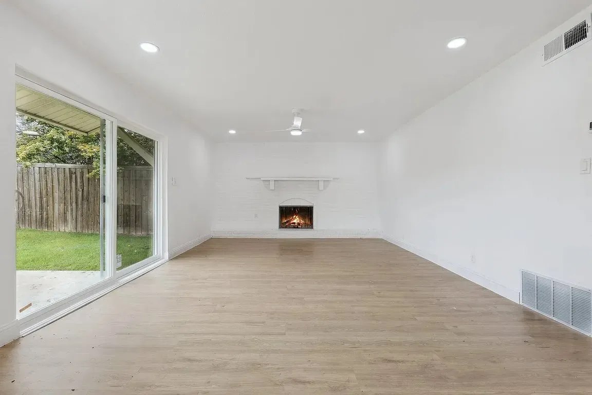 image 14 Bright living room with wood flooring, white walls, fireplace, and large sliding glass door to backyard.