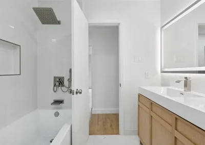 Modern bathroom with a bathtub, rain showerhead, large mirror, and wooden vanity with sink.