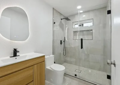 Modern bathroom with wood vanity, round mirror, glass shower enclosure, and wall-mounted showerhead.