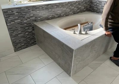 A modern tiled bathtub with a sunken tub, gray tiles, and a person standing nearby.