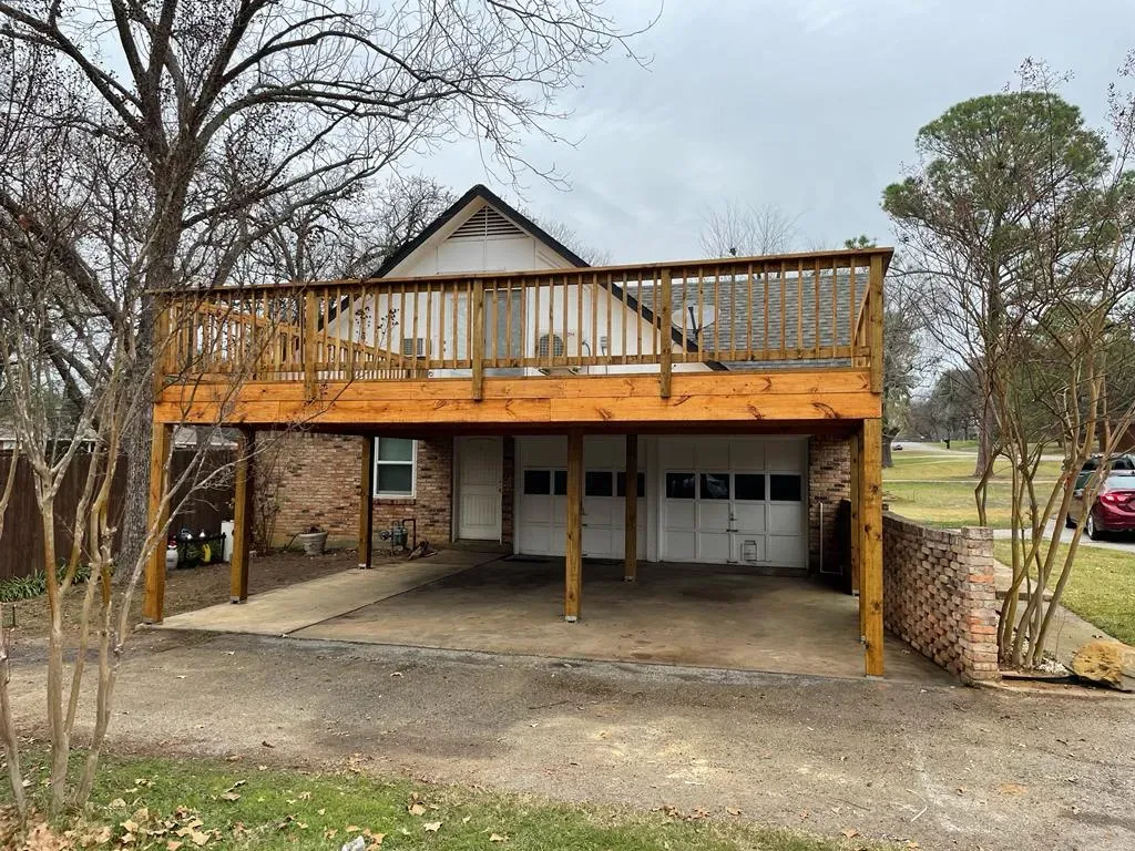 image 5 A house with a double garage and a large wooden deck built above the garage, surrounded by trees.