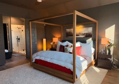 Modern bedroom with a wooden canopy bed, red and white bedding, and an ensuite bathroom visible in the background.