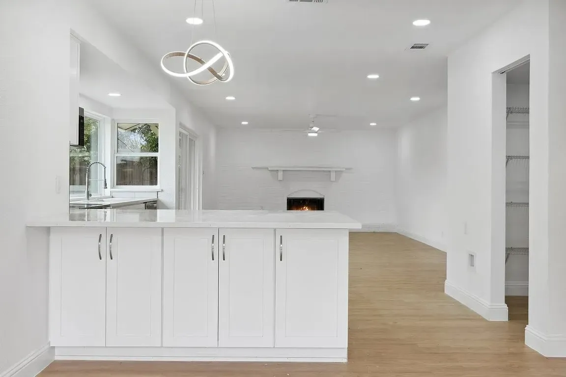 kitchen-2 Modern white kitchen with a breakfast bar, open shelves, and view into a living room with fireplace.