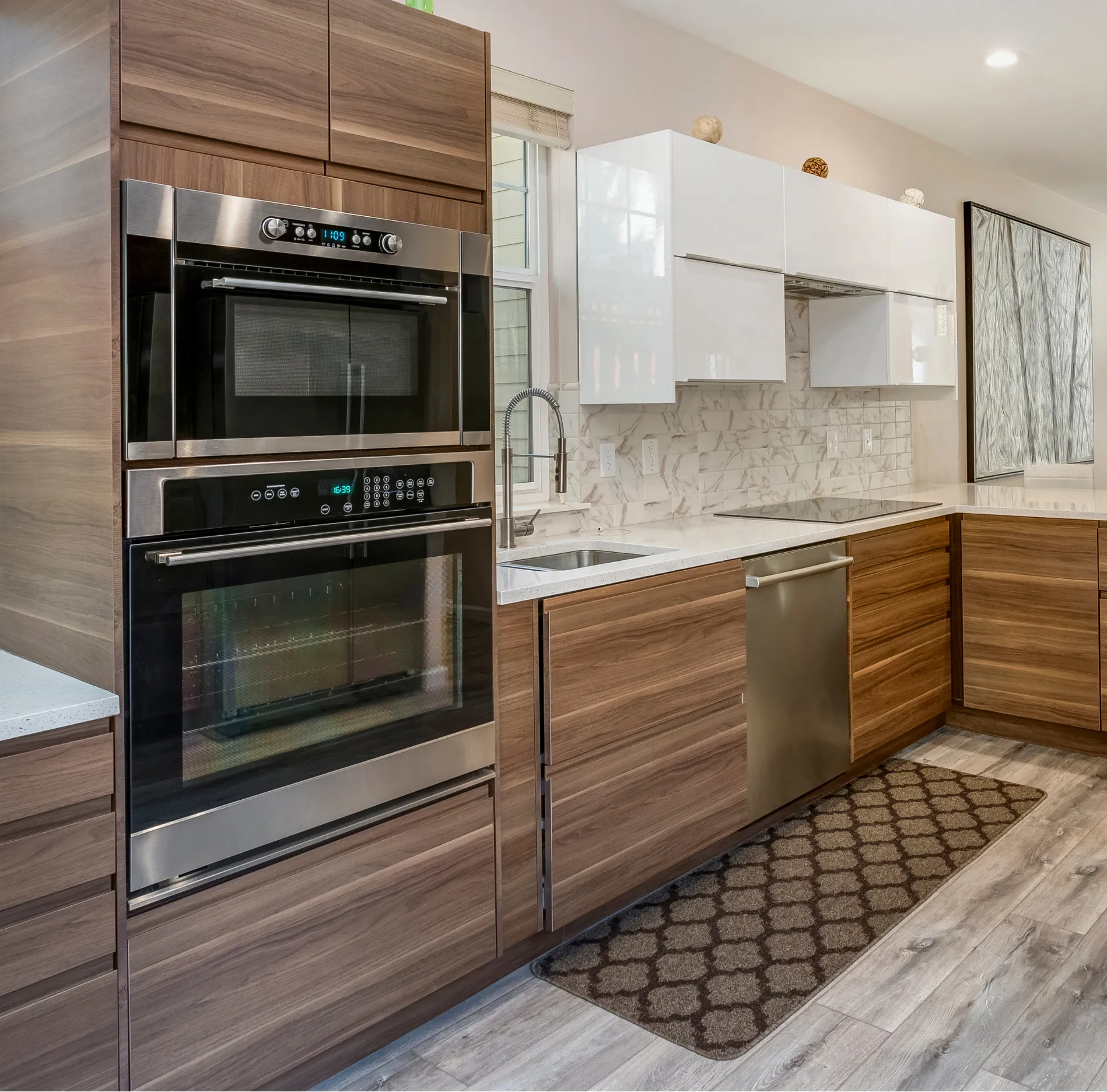 kitchen-3 Modern kitchen with wood cabinets, stainless steel appliances, white countertops, and a geometric floor mat.