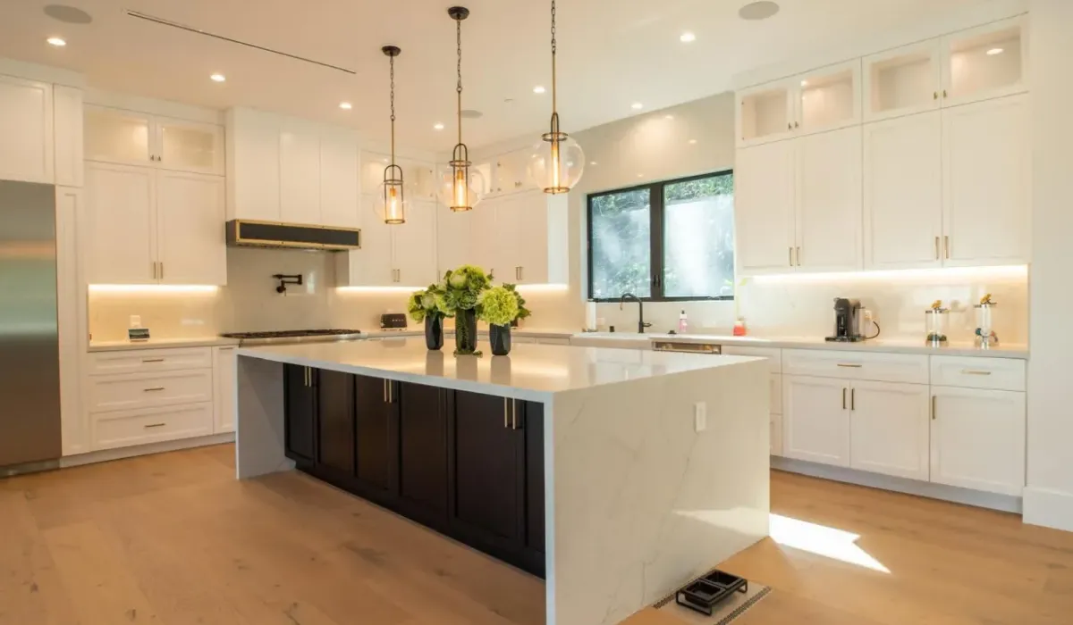 Modern kitchen with white cabinets, large island, pendant lights, and stainless steel appliances.