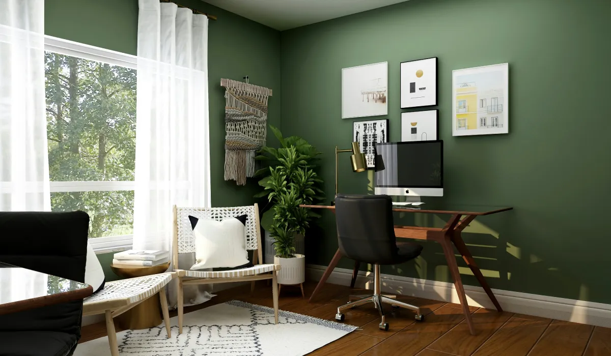 Modern home office with green walls, a desk, computer, black chair, and cozy seating by a large sunny window.