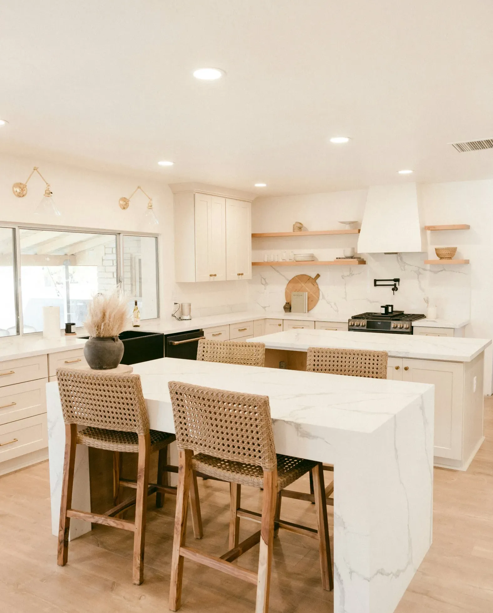 Bright, modern kitchen with marble island, rattan barstools, and light wood accents.